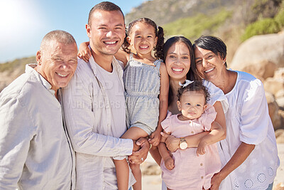 Portrait of smiling mixed race family with little girls standing together on beach. Adorable little kids bonding with mother, father, grandmother and grandfather outside
