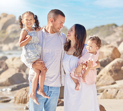 Buy stock photo A happy mixed race family of four enjoying fresh air at the beach. Hispanic couple bonding with their daughters while standing and carrying their daughters