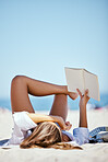 One beautiful young caucasian woman relaxing on the beach. Enjoying a summer vacation or holiday outdoors during summer. Taking time off and getting away from it all. Reading alone on the sand outside