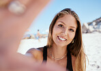 One beautiful young caucasian woman relaxing and taking a selfie photograph while sitting on the beach. Enjoying a summer vacation or holiday outdoors. Taking time off and getting away from it all