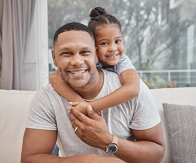 Handsome young mixed race man and his cute daughter hugging on a sofa in the living room at home. Father and his girl child bonding and showing affection. A single parent and female kid in the lounge