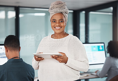 Portrait of confident young african american businesswoman browsing on a digital tablet device while working in an office with her colleagues in the background. Happy manager and supervisor planning online with smart apps