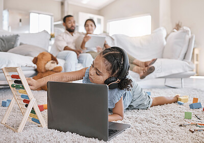 Closeup of a little cute girl using a laptop and wireless headphones while laying on the floor in the lounge. Hispanic girl using a wireless device to do her homework in the living room