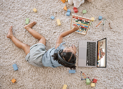 Buy stock photo Overhead view of a little cute girl using a laptop and wireless headphones while laying on the floor in the lounge. Hispanic girl using a wireless device to do her homework in the living room