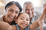 Portrait of smiling mixed race grandparents and granddaughter taking a selfie in the lounge at home. Hispanic senior man and woman taking photos and bonding with their cute little granddaughter at home