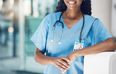 Closeup african american woman nurse smiling and leaning against a wall while standing in hospital. She\'s here to take care of her patients\' wellbeing. Health and safety in the field of medicine