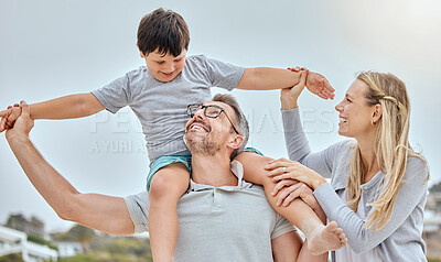 Happy caucasian family bonding together at the beach. Excited little boy sitting on his father\'s shoulders and holding his mother\'s hands while pretending to fly for play and fun. Loving parents relaxing with son outdoors