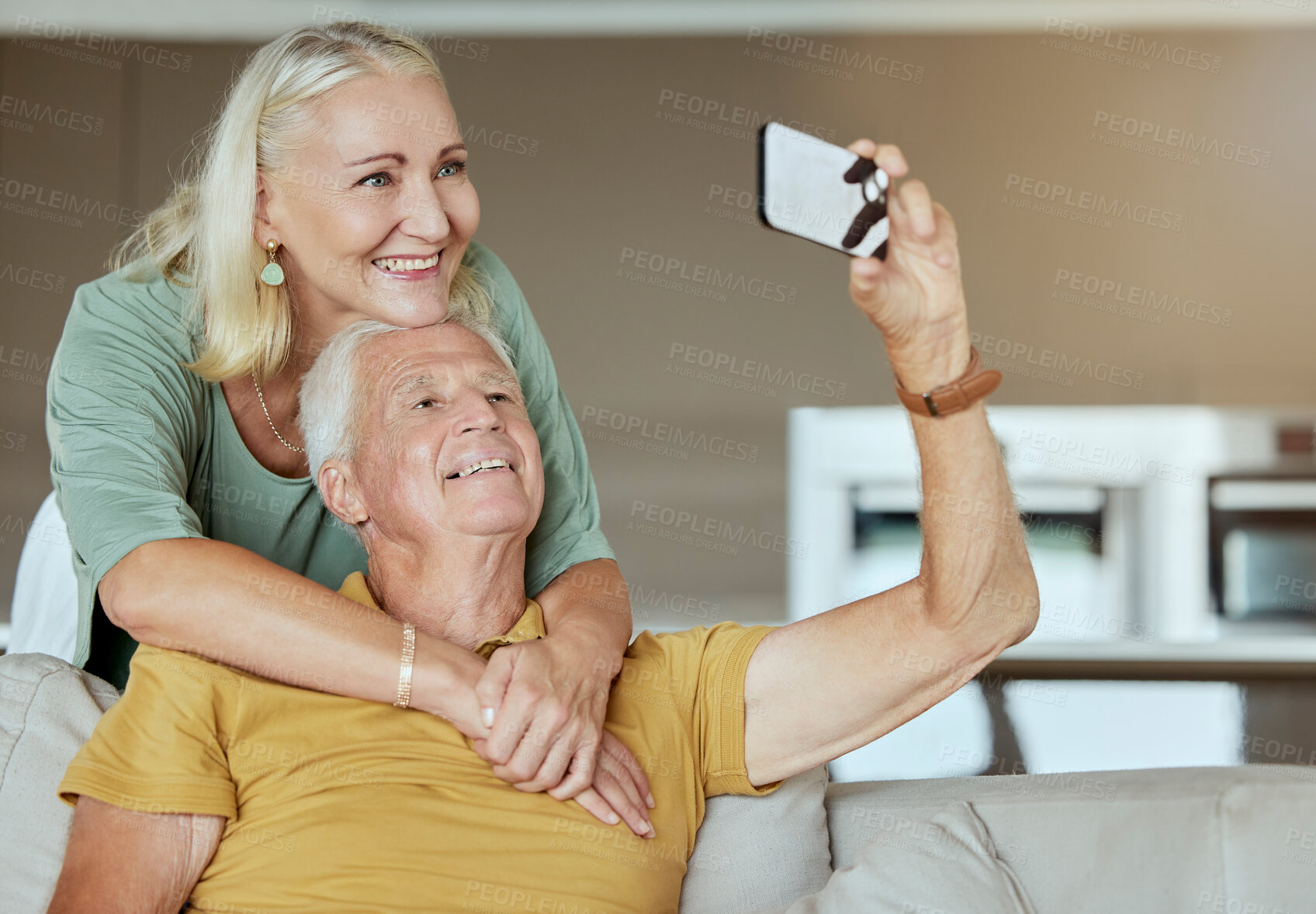 Buy stock photo Happy elderly couple bonding and enjoying retirement together. Senior caucasian man and woman being affectionate on a sofa at home  while taking selfies with a cellphone