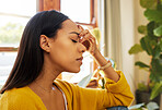 Stressed woman with a headache sitting at home in a bright living room with her hand against her head in front of a large window. Closeup side profile of one worried and anxious young female