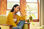 Tired hispanic woman at home sitting on a chair in a bright living room with her hand against her head in front of a large window. One worried and anxious young female inside with headache and stress