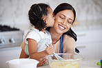 Happy mixed race mother and daughter baking and sharing a kiss while bonding. Young woman helping her daughter bake at home. Smiling mother holding an egg, cooking with her daughter. Happy little mixing a bowl of batter