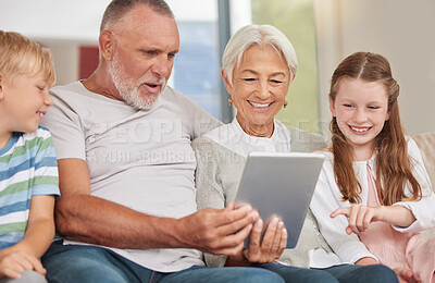 Buy stock photo A happy mature couple bonding with their grandchildren while babysitting and using a digital tablet at home. Grandparents relaxing with their cute little grandson and granddaughter browsing internet