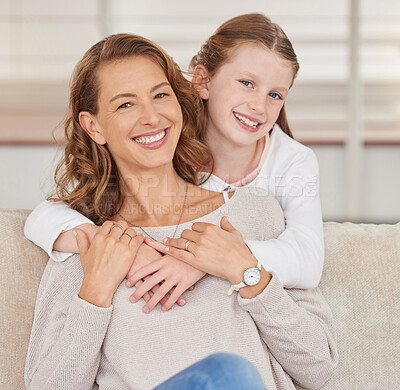 Portrait of a single mother and her daughter. Adorable girl bonding with her single parent and hugging in the living room at home. Smiling woman and her affectionate kid enjoying free weekend time