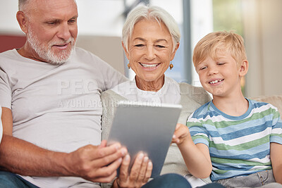 A happy mature couple bonding with their grandchild while babysitting and using a digital tablet on a couch at home. Grandparents relaxing with their cute little grandson and browsing the internet