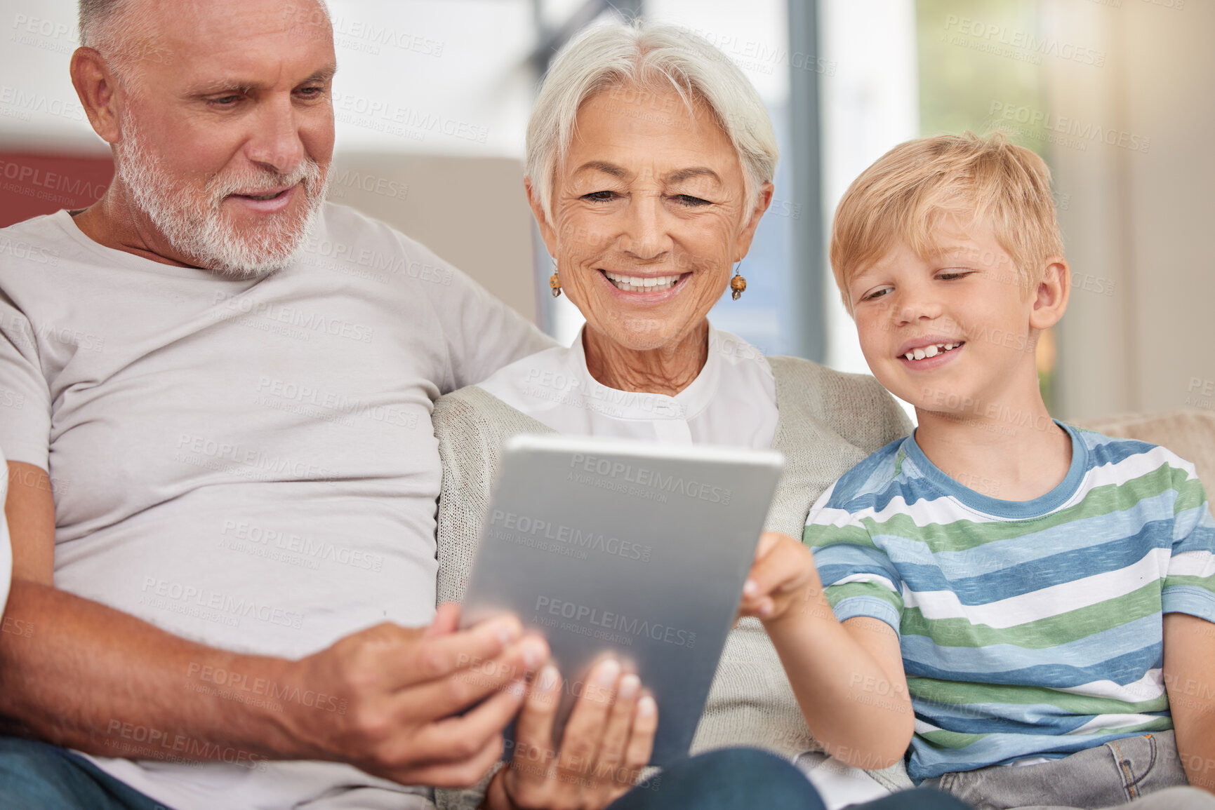 Buy stock photo A happy mature couple bonding with their grandchild while babysitting and using a digital tablet on a couch at home. Grandparents relaxing with their cute little grandson and browsing the internet 