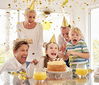 Buy stock photo Cheerful generational happy family wearing party hats while celebrating little girl's birthday with confetti and cake at home. Excited kids, parents and grandparent enjoying special surprise event