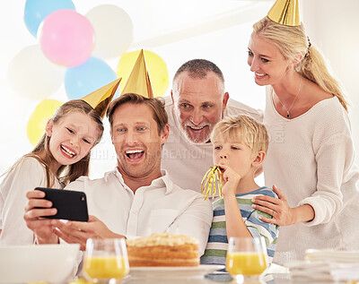 Buy stock photo A happy family celebrating a birthday with a party, wearing hats and taking a selfie using a phone. Mature man taking a photo of his father, wife and children at a party while making special memories