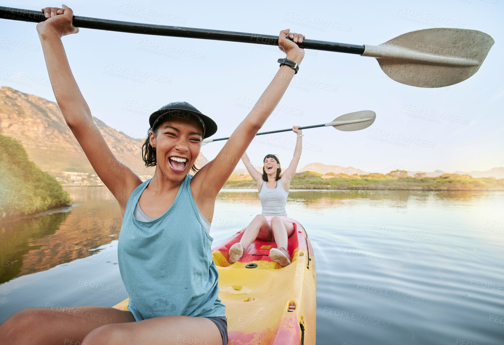 Buy stock photo Portrait two diverse young woman cheering and celebrating while canoeing on a lake. Excited friends enjoying rowing and kayaking on a river while on holiday or vacation. Winning on a weekend getaway