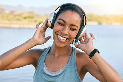 Excited woman smiling and listening to music while out on a lake. Happy young female enjoying nature and fresh air on a river outdoors. Using wireless headphones to stream or play music online