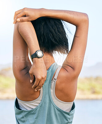 One active woman from the back stretching arms and triceps by pulling elbow  towards spine while exercising outdoors. Female athlete doing warmup to  prepare body and muscles for training workout or run