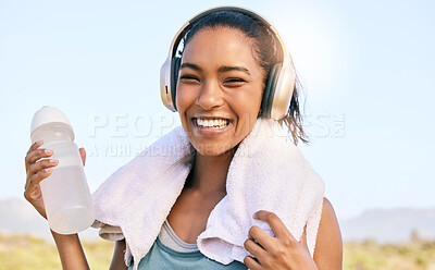Buy stock photo Excited woman smiling and listening to music while out for a workout in nature. Happy young female athlete with wireless headphones, water bottle and towel outdoors while exercising