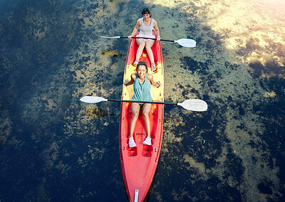 Above view of two smiling friends kayaking on the ocean together over summer break. Portrait of happy women canoeing and bonding outside in nature with water activity. Having fun on a kayak on weekend