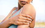 Closeup of an african american sportswoman suffering from shoulder pain while training. Woman holding her shoulder in pain while exercising outside. Overworking can lead to injury