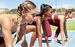 Three female athletes at the starting line in a track race competition at the stadium. Young sporty women in a race waiting and ready to run. Diverse sportswomen at the sprint line or starting blocks