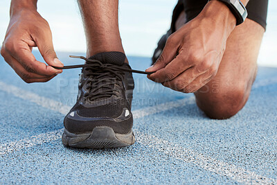 Buy stock photo Active athletic man preparing for a practice run to increase stamina for a competitive race on an Olympic track. Closeup of a fit african american athlete tying his shoelaces before running outside. 