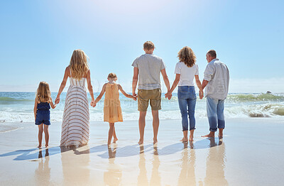 Buy stock photo Rear view of family holding hands and having fun on a beach vacation together on a sunny day. Relatives enjoying summer and sunshine, bonding and spending quality time walking and feeling ocean water