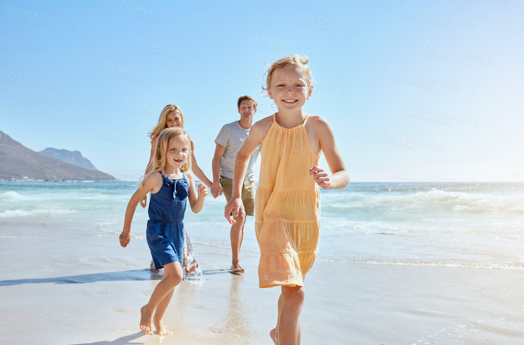 Buy stock photo Joyful young family with two children running on the beach and enjoying a fun summer vacation. Two energetic little girls having a race while their mother and father follow in the background