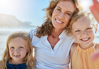 Cheerful mature woman and little girls taking selfies while on a beach vacation. Happy little girls smiling and sitting with foster or adopted mom, grandma or foster parent, enjoying fresh summer air