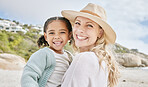 Portrait of a mature mother and her mixed race cute little daughter smiling and standing on the beach smiling. Woman and her girl bonding on a day out in the sun