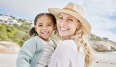 Buy stock photo Portrait of a mature mother and her biracial innocent little daughter smiling and standing on the beach smiling. A happy woman and her adopted girl bonding on a day out during a summer vacation 