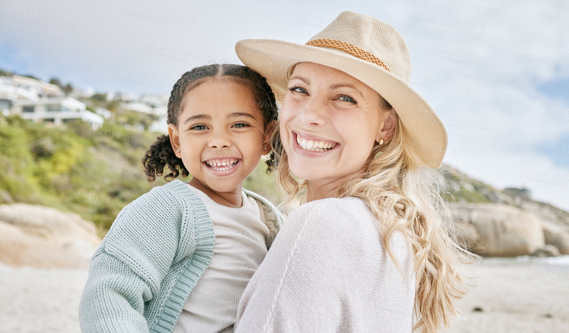 Buy stock photo Portrait of a mature mother and her biracial innocent little daughter smiling and standing on the beach smiling. A happy woman and her adopted girl bonding on a day out during a summer vacation 