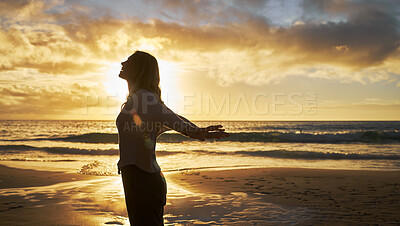 Buy stock photo Silhouette of a woman on the beach at sunset outside. Profile of female stretching her arms behind her at the seaside feeling free. Relaxed woman enjoying a seaside sunrise on vacation with copyspace