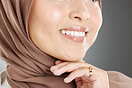 A glowing beautiful muslim woman isolated against grey copyspace background. Young woman wearing a hijab or headscarf showing her natural looking veneers after getting a teeth whitening treatment