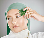 A glowing beautiful muslim woman isolated against grey copyspace background. Young woman wearing a hijab or headscarf, using a gua sha to reduce wrinkles and promote cell renewal, anti ageing tool