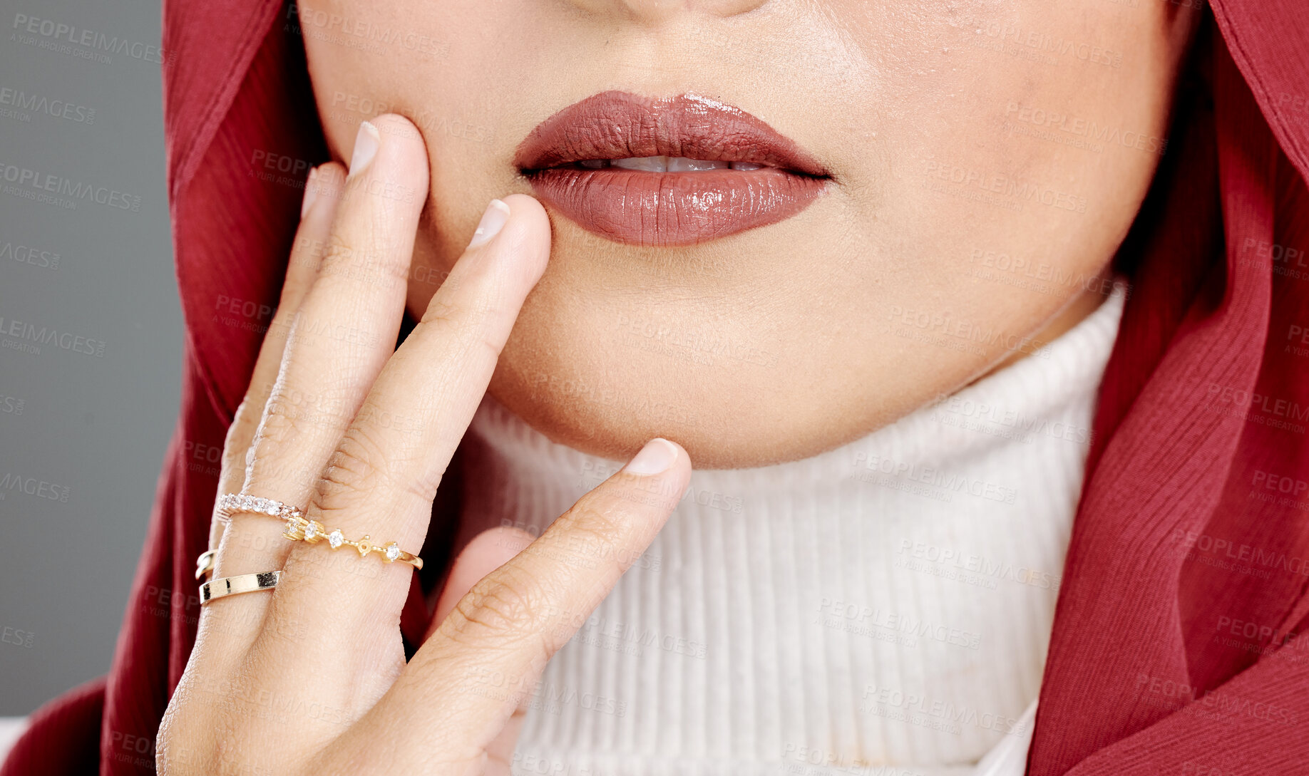 Buy stock photo Muslim woman wearing rings, lipstick, a hijab, touching her face and posing in studio. Closeup of half headshot of a confident arab model isolated against grey background. Fashionable middle eastern