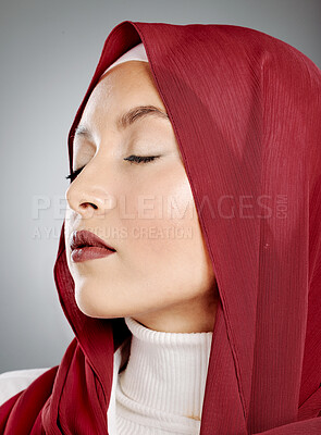 Closeup of a glowing beautiful muslim woman isolated against grey studio background. Young woman wearing a red hijab or headscarf showing her eyelash extensions and jewellery. Touching flawless skin