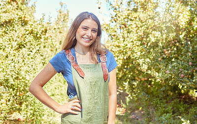 Female farm worker in an orchard standing on a fruit farm during harvest season. Portrait of a young smiling farmer between fruit trees on a sunny day. The agricultural industry growing fresh produce