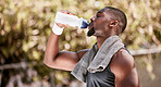 Athlete drinking water from a bottle during an outdoor workout. Fit, athletic and active african american taking break to hydrate and refresh while standing alone outside. Routine exercise for health