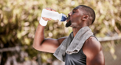 Athlete drinking water from a bottle during an outdoor workout. Fit, athletic and active african american taking break to hydrate and refresh while standing alone outside. Routine exercise for health