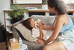 Girl, child or female suffering from a flu, covid or cold while laying on the couch at home. Loving, caring and kind mother taking care of her sick, ill or unwell daughter by blowing her nose