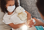 Top view portrait of a child weaning a surgical disposable mask applying antibacterial sanitizer spray by her mother. Parent is helping to protect the spread of corona virus outbreak at home