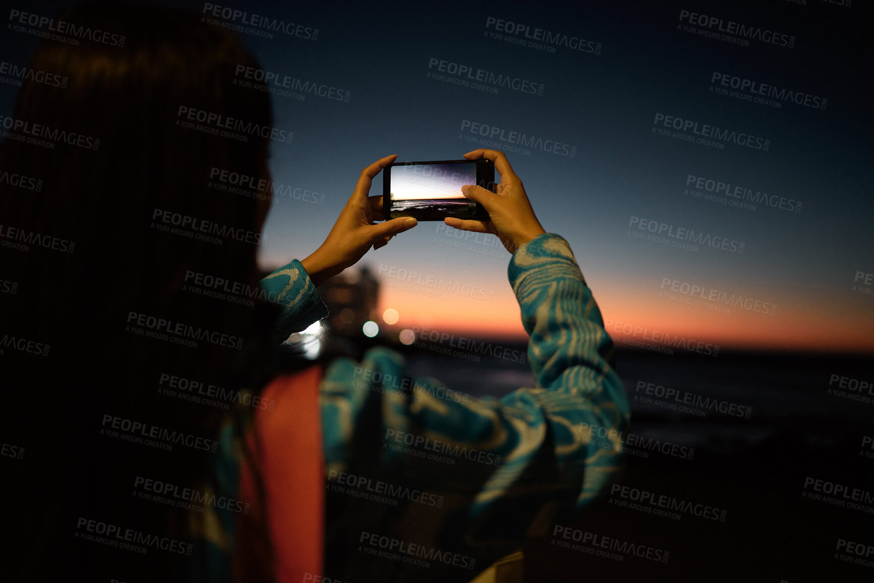 Buy stock photo Trendy tourist taking photo on her phone of the ocean with beautiful sunset on the horizon at night outdoors. Influencer or vlogger taking picture of nature sea view to post or share on social media