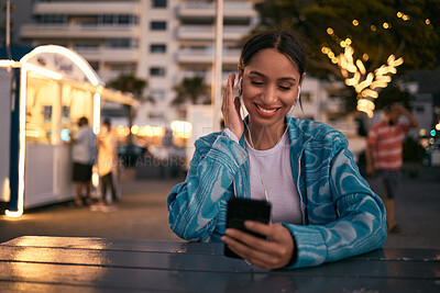 Modern, trendy and happy woman texting on a phone, listening to music and smiling while browsing social media at at an outdoor cafe. Young female enjoying night life in the city while chatting online