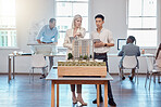 Business professionals in the field of architecture discuss building designs in a modern office. A pair of male and female architects converse over a model prototype for an upcoming project.