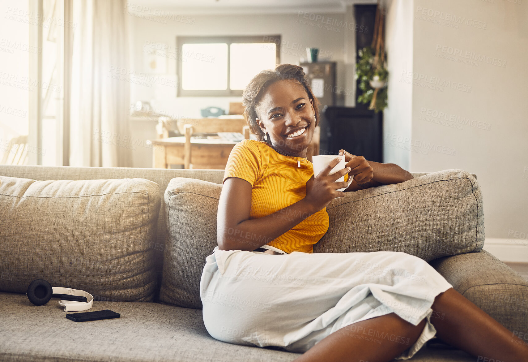 Buy stock photo Beautiful, pretty and happy woman relaxing, drinking coffee and resting on the couch in the living room alone at home. Portrait of a smiling, cheerful and joyful black female enjoying a warm drink