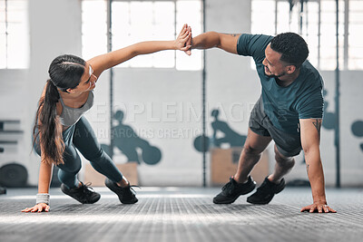 Healthy, fit and active gym partners exercising together and doing pushups with a high five. Boyfriend and girlfriend training and exercising in a health facility as part of their workout routine